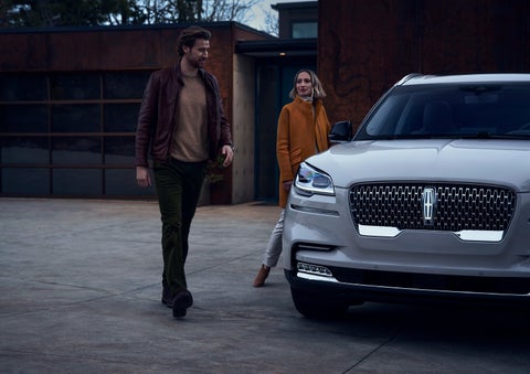 A man and a woman approaching a 2024 Lincoln Aviator® SUV, which illuminates certain lights when they are close | Oliver Lincoln in Plymouth IN