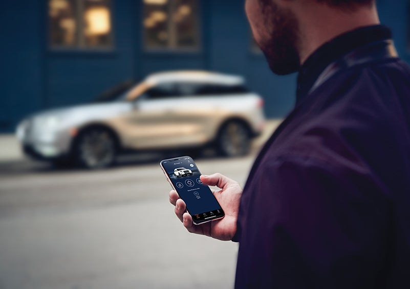 A person is shown interacting with a smartphone to connect to a Lincoln vehicle across the street. | Oliver Lincoln in Plymouth IN